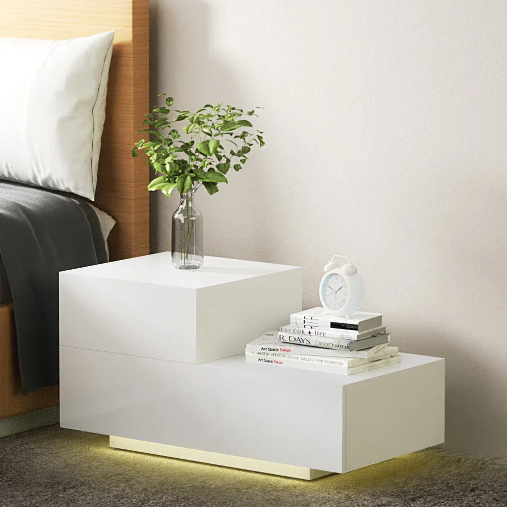 Modern white LED bedside table with books, alarm clock, and plant in a glass vase